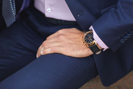 A view of the mans hand with a black clock on the background of a blue mans suit.の写真素材