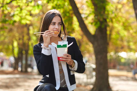 Smiling brunette girl is testing Chinese egg noodless in the park on the nature background.の写真素材