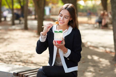 Smiling brunette girl is testing Chinese egg noodless in the park on the nature background.の写真素材