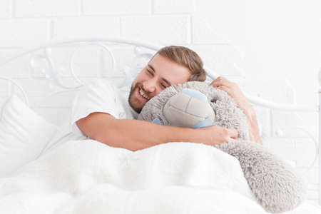Young man lying in bed with a teddy bear