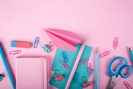 Notebooks, pens, pink paper airplane, scissors, paper clips, rulers of blue and pink colors next to each other on a pink background. Copy space. Close-up of console devices.の写真素材