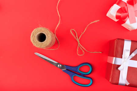 Gift boxes on a red surface. Branch of Christmas tree, ribbons, bow, scissors, cones and a ball of brown threads lie on a red background.の写真素材
