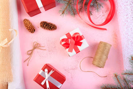 Gift boxes on a pink surface. Branch of Christmas tree, ribbons, bow, cones and a ball of brown threads lie on a pink background. Close-up of gifts.の写真素材