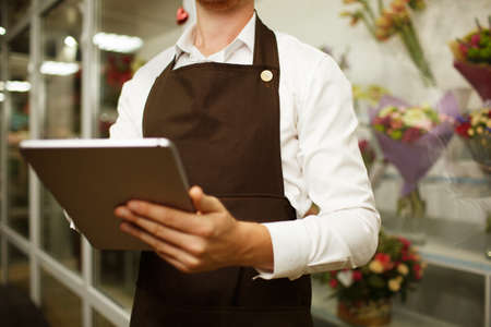 Close-up florist working on tablet on a blurred background. Progressive small business concept.の写真素材