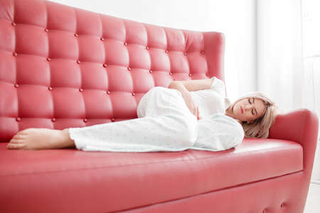 The girl lies on a bed with a pain in the stomach on a white backgroundの写真素材