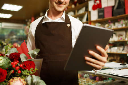 Close-up florist working on tablet on a blurred background. Progressive small business concept.の写真素材