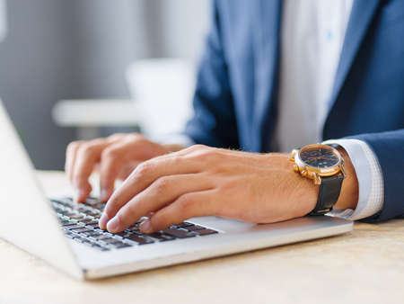 Close-up mans hands working on a wireless laptop on a blurred background. Digital design concept.の写真素材