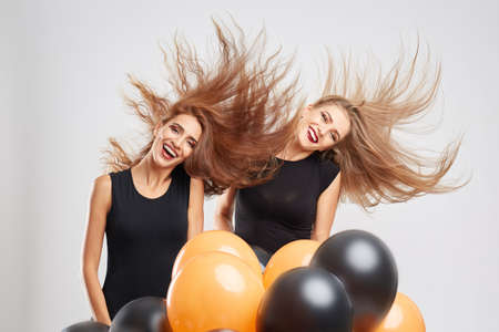 Happy festive girls waving hair around with balloons on a light background. Halloween fun concept.の写真素材
