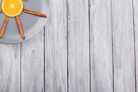 A piece of orange in a gray plate with cinnamon on a wooden table.の写真素材