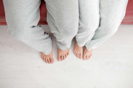 Legs of a man and a girl in white pants hang from a red sofa on topの写真素材