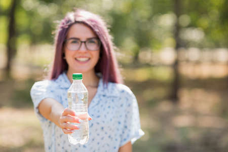 Happy cute girl holding a bottle of water on a blurred background. Stay hydrated concept. Copy space.の写真素材