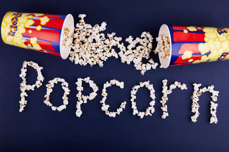 The word popcorn is scattered on a blue background. On top are two boxes of popcorn. Close-up. View from above. The concept is cinema.の写真素材