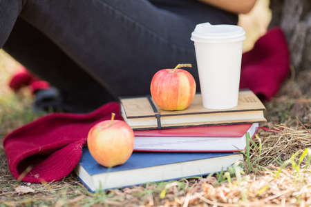 Close-up of a female student sitting next to textbooks, cup of hot coffee and apple on a blurred natural background. Modern student habits concept.の写真素材