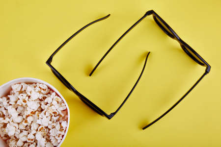 Bowl with popcorn and 3D glasses on a yellowbackground top viewの写真素材