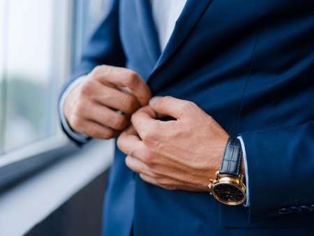 Close-up of a businessman in a stylish formal wear on a blurred window background. Macro of rich man in a suit with a watch. Copy space.の写真素材