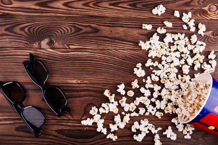 Bowl with scattered popcorn and pair 3D glasses on a wooden backgroundの写真素材