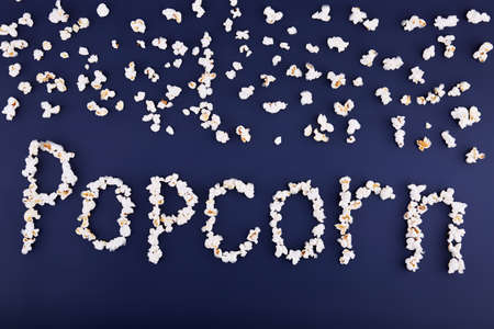 The word popcorn is scattered on a blue background. Top of popcorn. Close-up. View from above. The concept is cinema.の写真素材