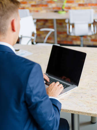 Close-up of a busy office worker typing on a wireless laptop on a light desk background. Man using laptop with blank screen.の写真素材