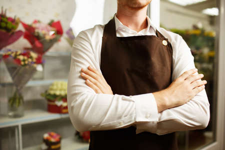 Close-up of a professional florist male wearing a traditional white and brown uniform with an apron on a blurred florist shop background.の写真素材