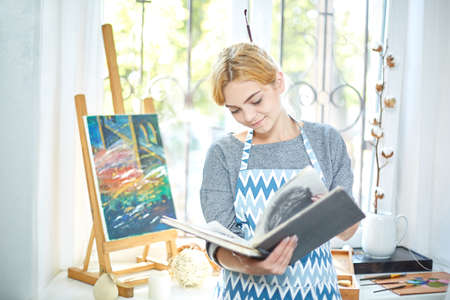 Pretty blode girl looking on a album and smiling. Art concept,の写真素材