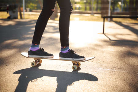 The legs of a skateboarder girl in sneakers do a trick on a skateboard in a park in the fresh air. Close-up.の写真素材