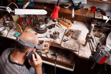 Close-up of a mature jewelry craftsmen making accessory on a messy workshop background. Unique jewelry making equipment and tools.の写真素材