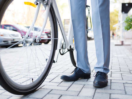 Close-up of a formal man standing next to a bicycle on the light urban background. Ecologically-friendly modern transportation concept.の写真素材