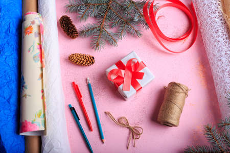 Top view of composition of a present wrapping on a pink table background. Christmas gift next to pencils, rope and winter decorations.の写真素材