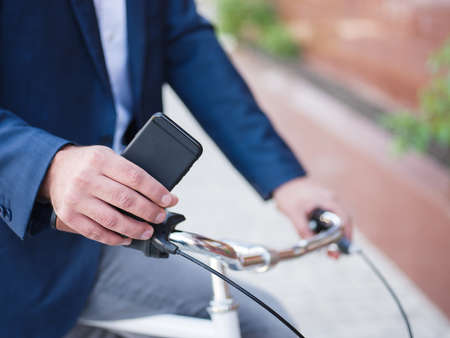 Businessman in blue suit on a bicycle, phone close-up with his hands on a blurred backgroundの写真素材