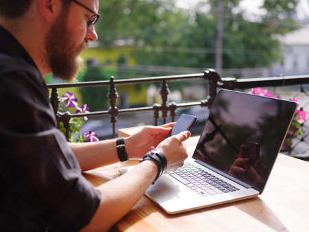 A man sitting at a wooden table is holding a telephone. On the desk is a laptop.の写真素材