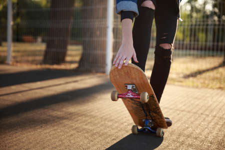 The legs of a skateboarder girl in sneakers do a trick on a skateboard.