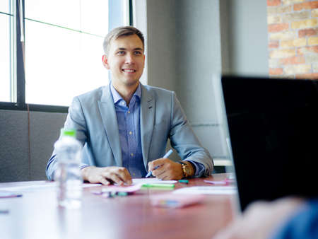 Young man in suit, at desk in office. Close-up of a bottle of water.の写真素材