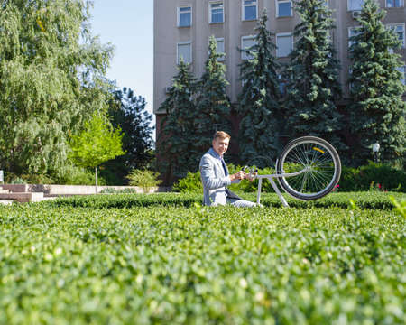 A young guy raises his bicycle on the rack in the garden of the administrationの写真素材