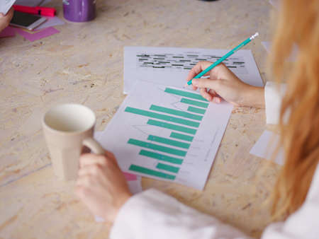 A girl with a coffee and pencil in the other hand looks at the company's work schedule. A businesswoman with paper.の写真素材