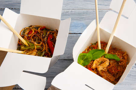 Noodles with vegetables in a white box for export to a wooden gray table. Two portions. Two sets of Chinese sticks. Close-up. View from above.の写真素材
