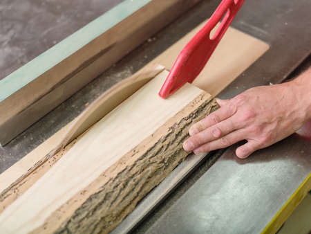 The joiner saws the timber beam on the circular saw and holds the bar with a special device close-up...