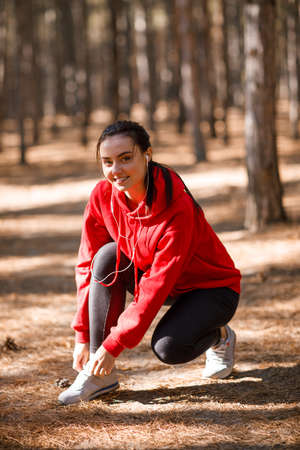 Girl tying shoelaces in the forest during training. Concept photo, close-upの写真素材
