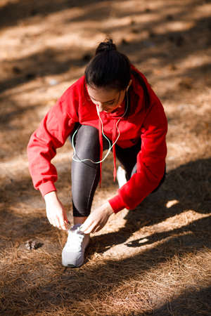 Girl tying shoelaces in the forest during training. Concept photo, close-upの写真素材