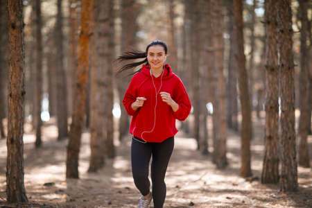 Young brunette athlete runs in the autumn forest.の写真素材