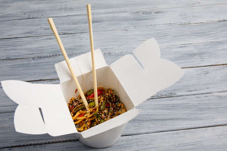 Noodles with vegetables in a white box for export on a wooden gray table. Close-up. View from above.の写真素材
