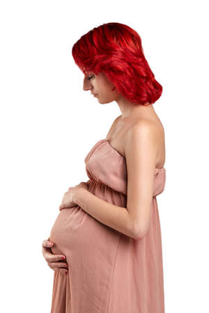 A pregnant young woman with red hair in a pink dress.の写真素材