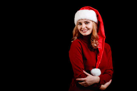Beautiful happy festive girl in a santa cap on a black background. Christmas costume concept. Copy...