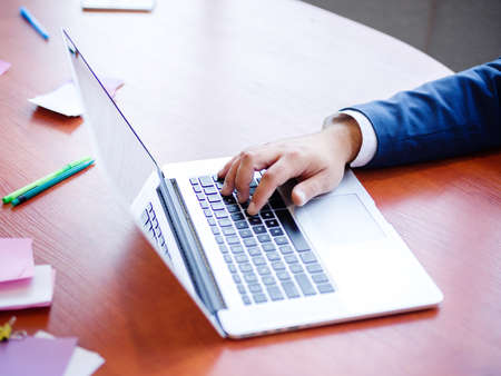 Hands of a businessman in a white shirt and blue jacket behind a laptop working on future ideas