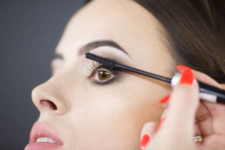 A beautiful young girl makeup artist paints eyelashes.