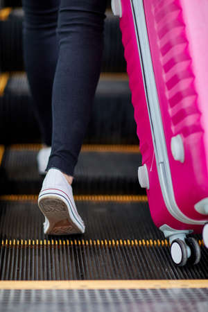 The girl raises a pink suitcase on the escalatorの写真素材