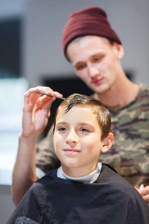 Hairdresser in barbershop makes a haircut for a young guyの写真素材
