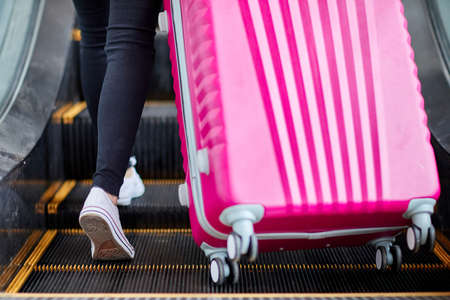 The girl raises a pink suitcase on the escalatorの写真素材