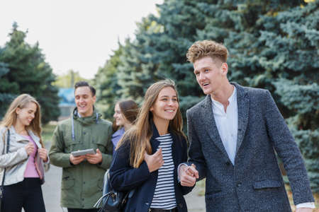 Young couple walking with friends. The guy holds the girls hand.