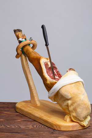 Whole jamon on a wooden stand and wooden table open from cloth and knife inside. Traditional Spanish food, Mediterranean food. Dried pork leg, salted pork hoof. Full size vertical image.の写真素材