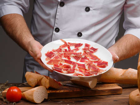 Thinly sliced jamon, on a white plate. Cold smoked meat plate with pork, prosciutto, on a white plate. A set of wine appetizers. Italian, Spanish food. Horizontal image.の写真素材